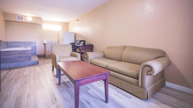 A living room with a sofa, a coffee table, and a small table with a chair. - Crossroads Hotel and Suites Irving (Irving)
