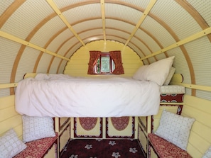 A bunk bed with a canopy, a window with curtains, and patterned bedding. - The Bowtop Gypsy Caravan (Eye)