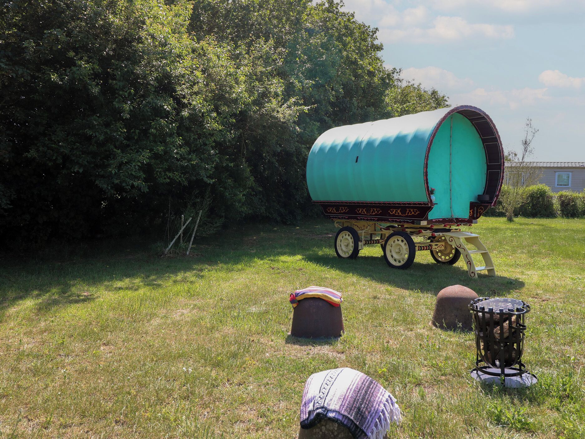 Een overdekte wagen met een turquoise hemelkleed, een houten bank en een metalen grill in een grasveld.