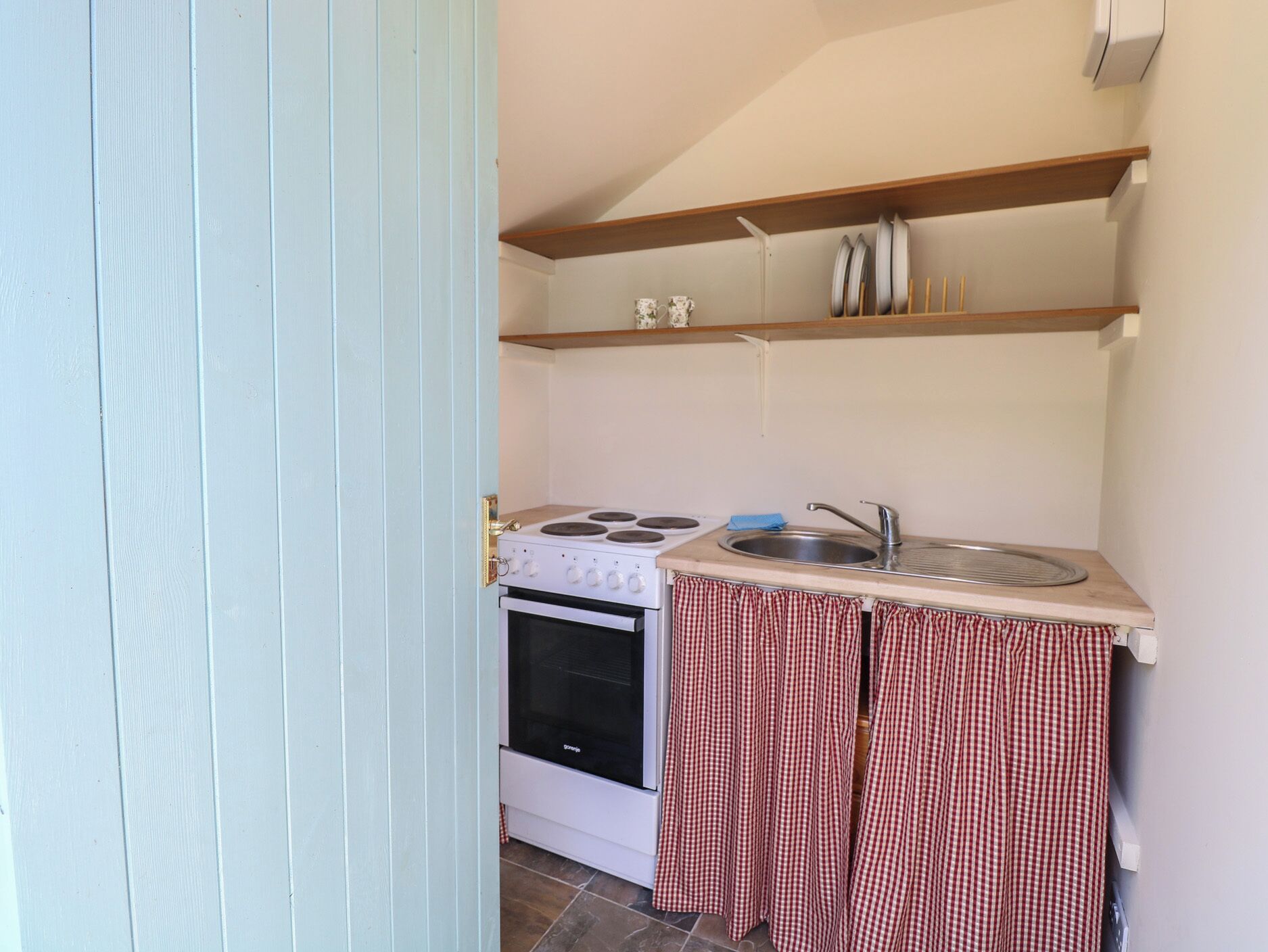 A compact kitchen with a stove, oven, sink, and a small shelf above the counter.