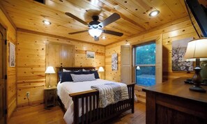 Ein Schlafzimmer einer Holzhütte mit Bett, Nachttischlampen, Deckenventilator und Fenster.