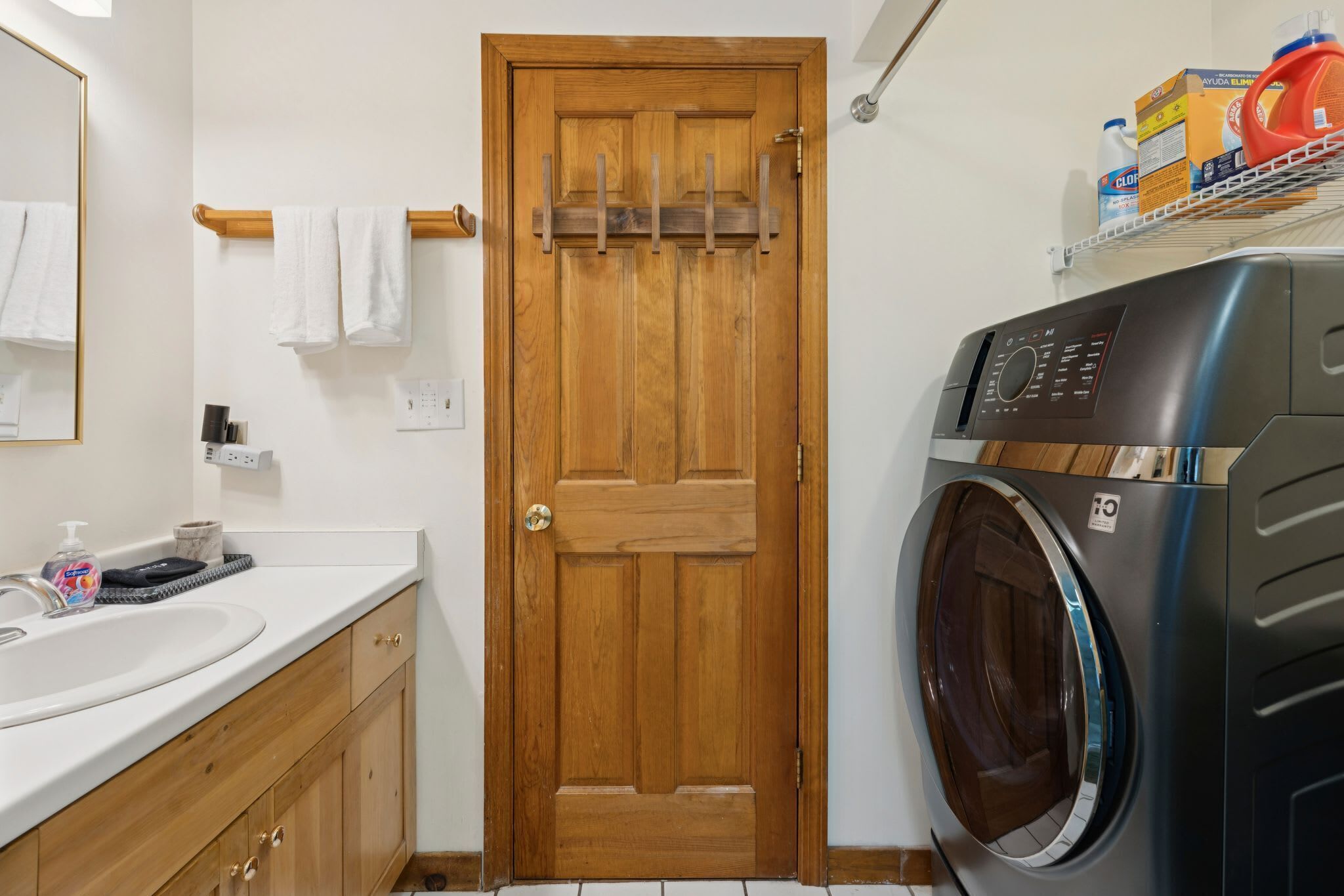 Une salle de bain avec une porte en bois, un lave-linge, un évier et un miroir.