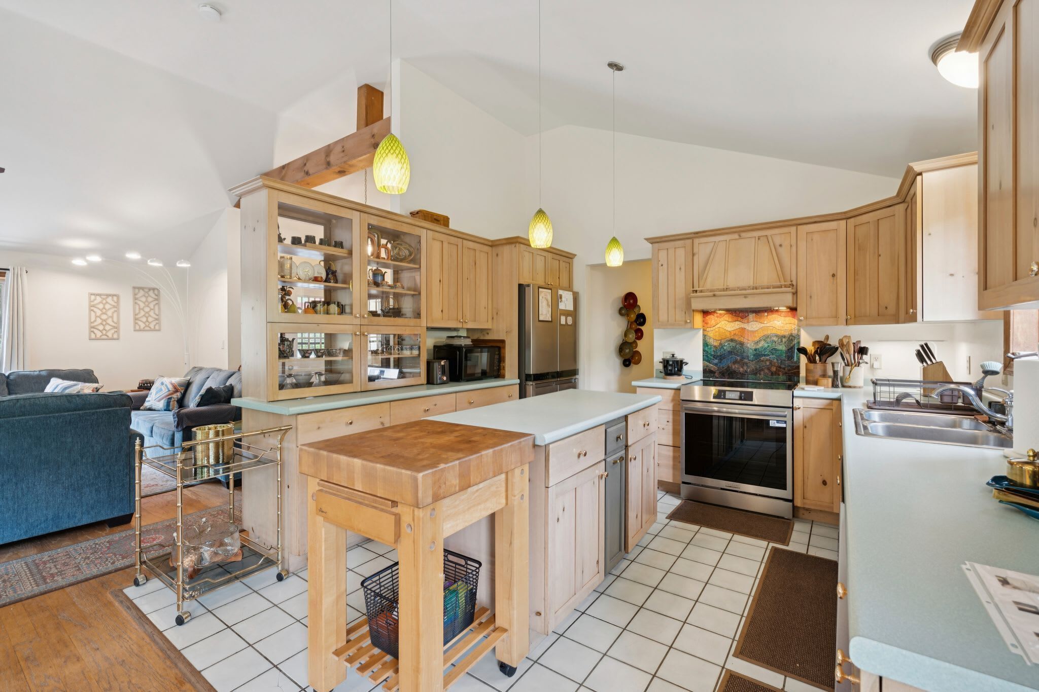 Une cuisine moderne avec des meubles en bois, un îlot central, des appareils électroménagers en acier inoxydable et des luminaires suspendus.