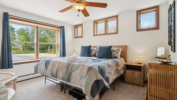 Une chambre à coucher comprenant un lit, un ventilateur de plafond, une table de chevet, une commode et de grandes fenêtres.
