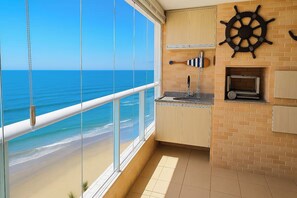 A kitchen with a view of the ocean, a ship's wheel decoration, and a small island with a sink.
