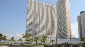 Dos edificios altos con balcones, cielo despejado y palmeras al frente.