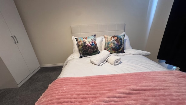 Ein Hotelzimmer mit einem Bett, zwei Kissen, einer rosa Decke und einem Kleiderschrank.