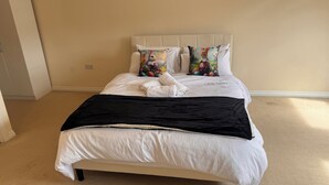 Ein Schlafzimmer mit einem Bett, weißer Bettwäsche, zwei Zierkissen, einer schwarzen Tagesdecke und einem weißen Handtuch.