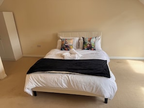 A bedroom with a bed, white bedding, two decorative pillows, a black throw blanket, and a white towel.