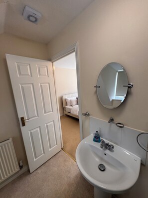 A bathroom with a white sink, a mirror, and a door leading to a bedroom. - Sleeps 9- Garden-Parking-WiFi Near uea and Nnuh (Costessey)