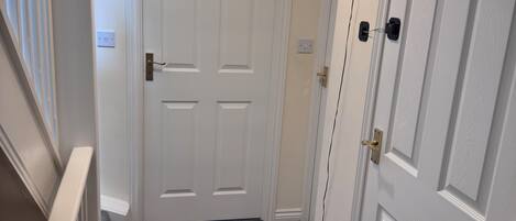 A hallway with a carpeted floor, white doors, a light fixture, and a thermostat on the wall.
