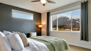 Ein Schlafzimmer mit einem Bett, einer Stehlampe, einem Deckenventilator und einem großen Fenster mit Blick auf die Berge.