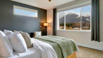 A bedroom with a bed, a standing lamp, a ceiling fan, and a large window with a mountain view.
