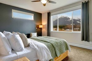 Ein Schlafzimmer mit einem Bett, einer Stehlampe, einem Deckenventilator und einem großen Fenster mit Blick auf die Berge.