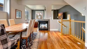 Ein modernes Wohnzimmer mit Kamin, Holzboden, Essbereich mit Stühlen und Treppe mit Geländer.