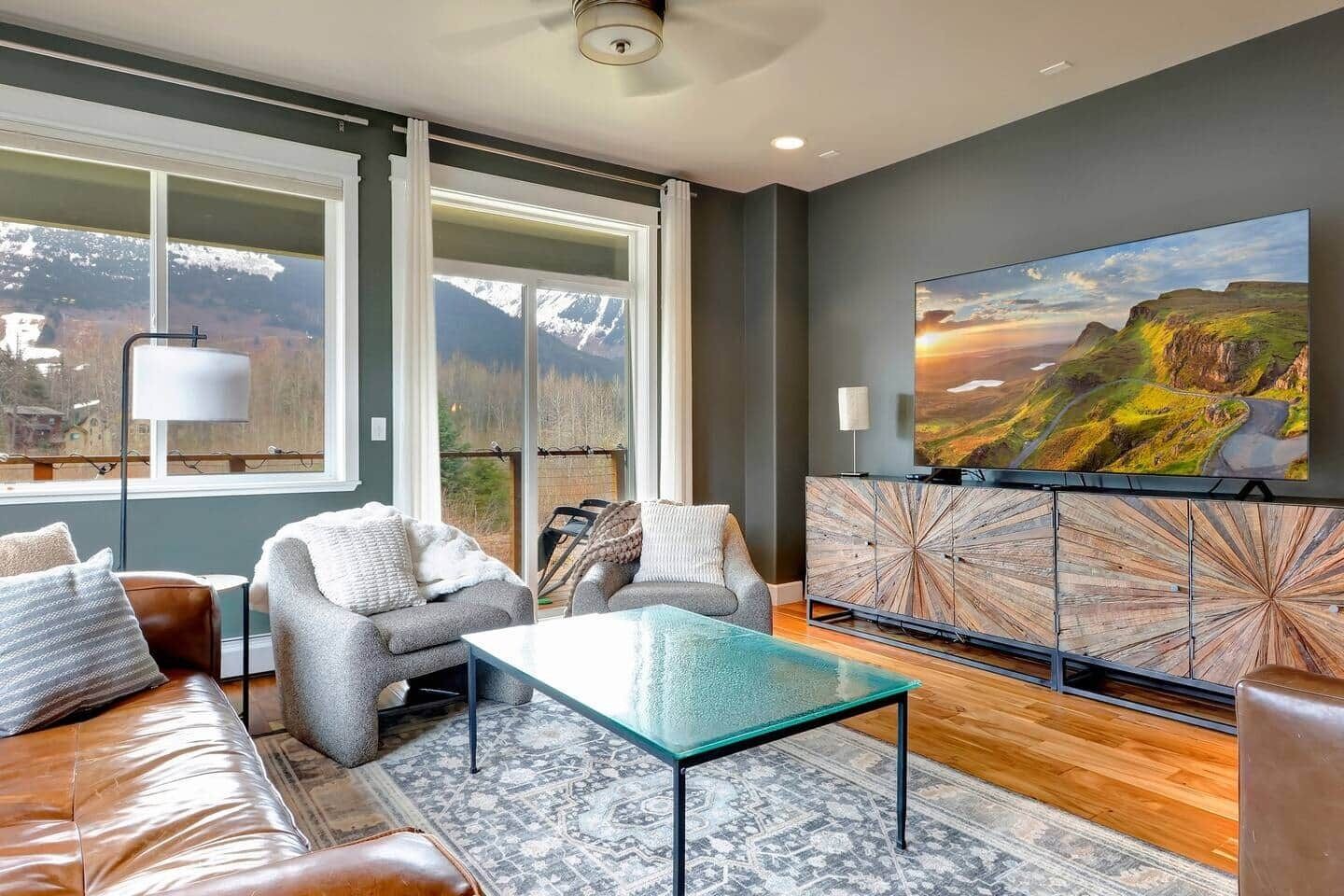 A modern living room with a sofa, armchairs, a glass coffee table, and a large TV on a wooden cabinet.