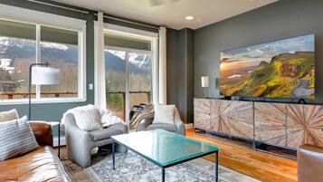 A modern living room with a sofa, armchairs, a glass coffee table, and a large TV on a wooden cabinet.