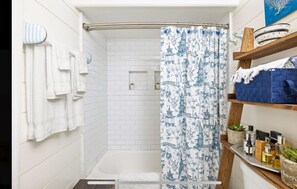 Een badkamer met douchegordijn, witte betegelde wanden, een handdoekhouder en een plank met toiletartikelen.