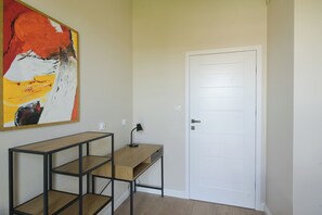 A room with a white door, a desk with a lamp, and a large abstract painting on the wall. - Apartment Aurora by Q4 Apartments  (Gdańsk)