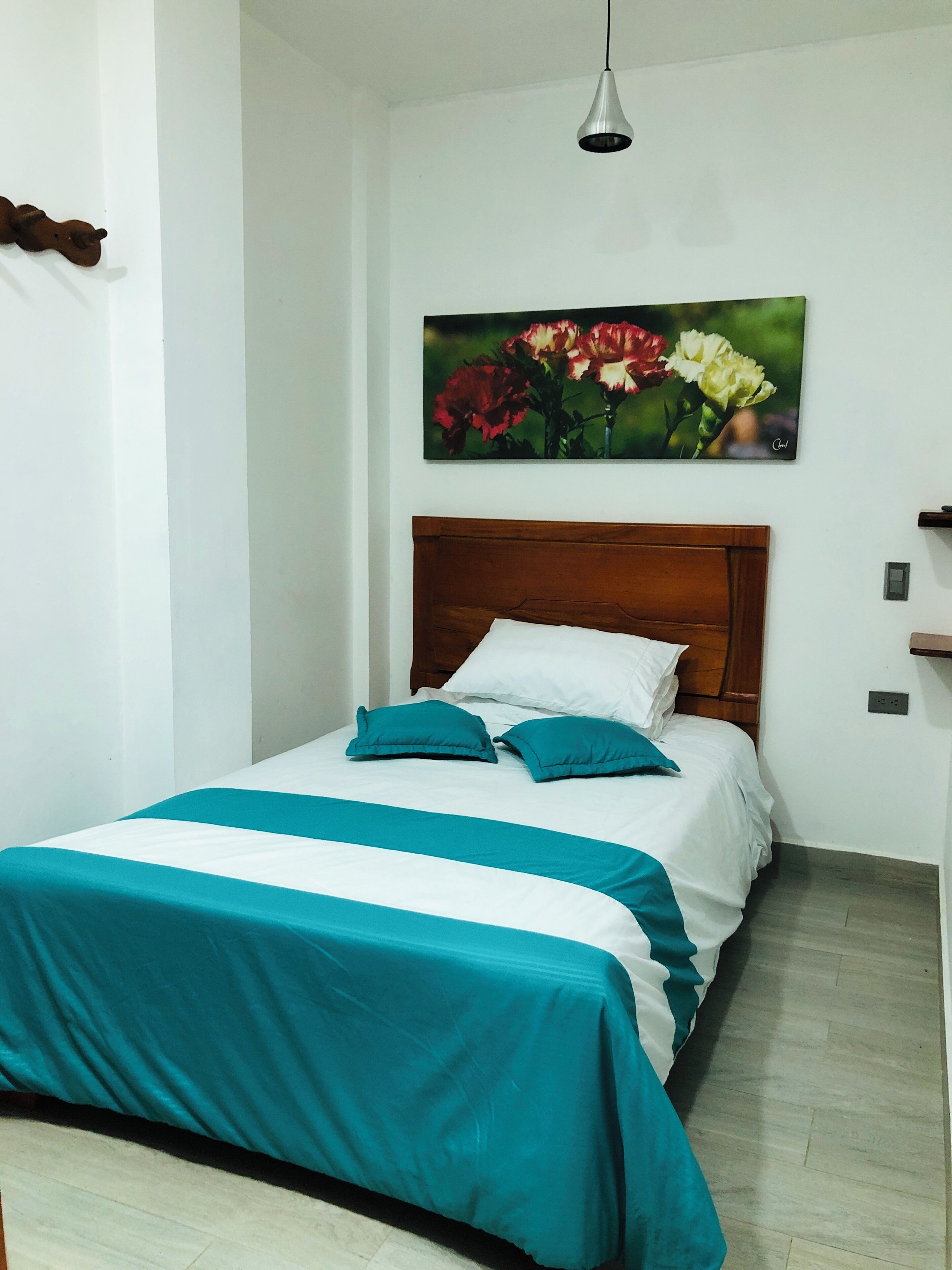 A neatly made bed with a wooden headboard, a teal and white bedspread, and two teal pillows.