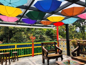 A covered outdoor seating area with colorful umbrellas, wooden chairs, and a tiled floor. - 40 Amigos Hotel (Jardin)