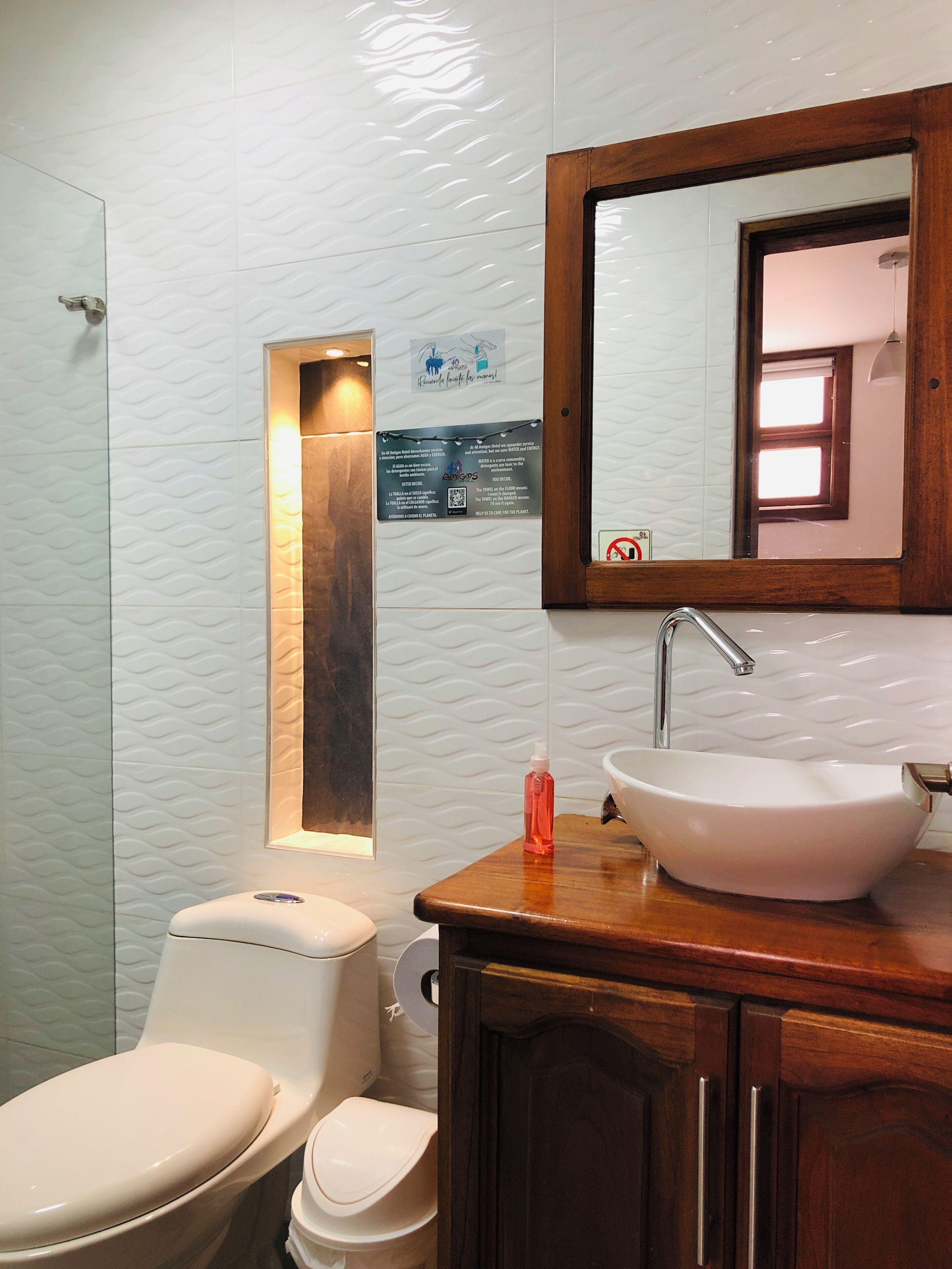 Un baño con lavamanos blanco, tocador de madera y un espejo.