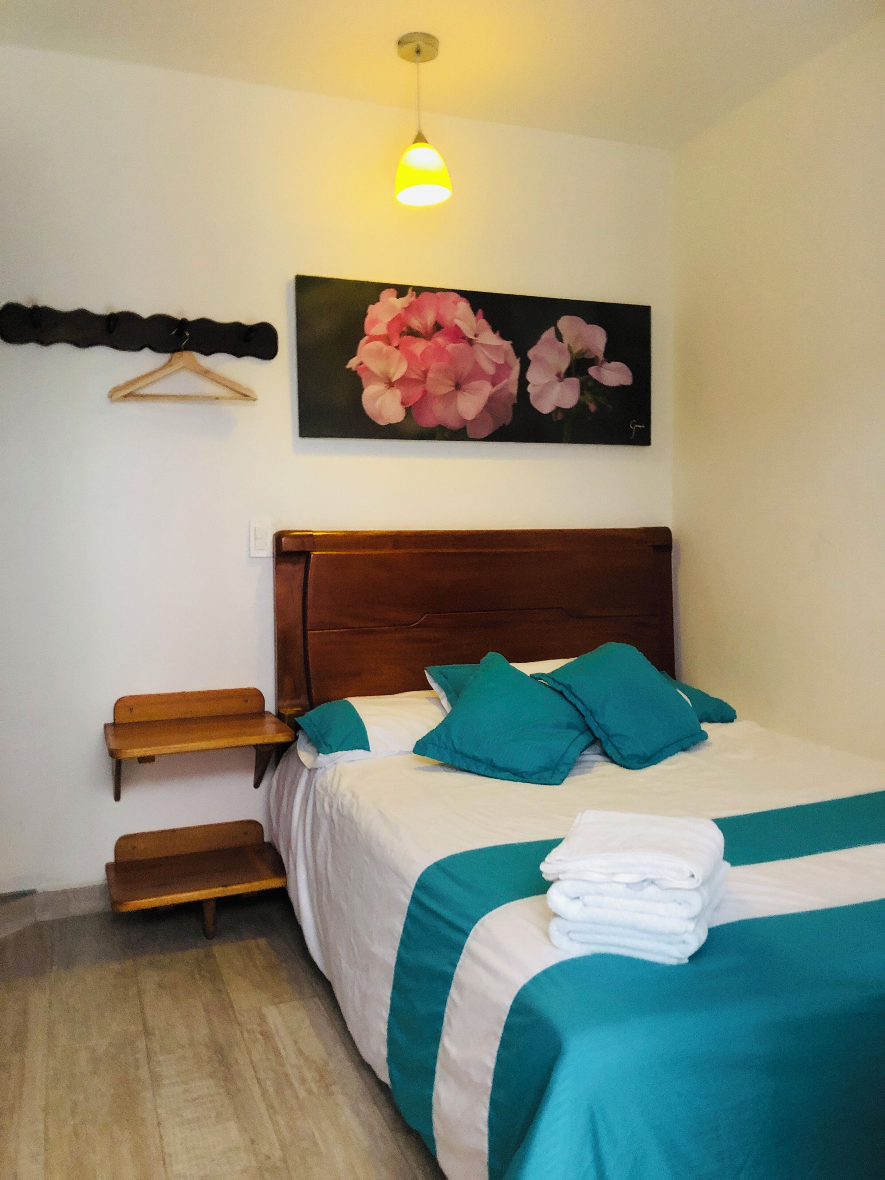 Quarto com cabeceira de madeira, cama com roupa de cama verde-água, pintura de flores na parede e um banco de madeira.