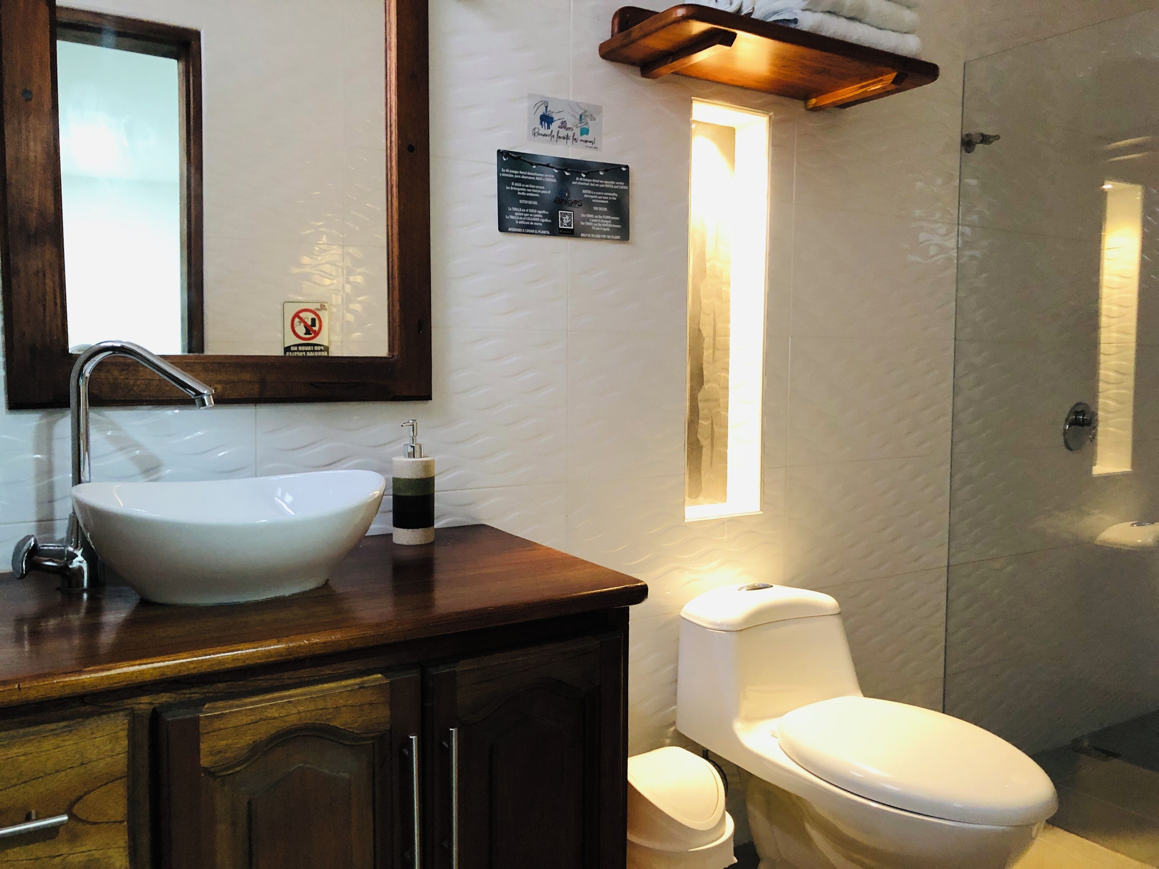 A bathroom with a white sink, a mirror, a wooden cabinet, a toilet, and a wall-mounted light fixture.