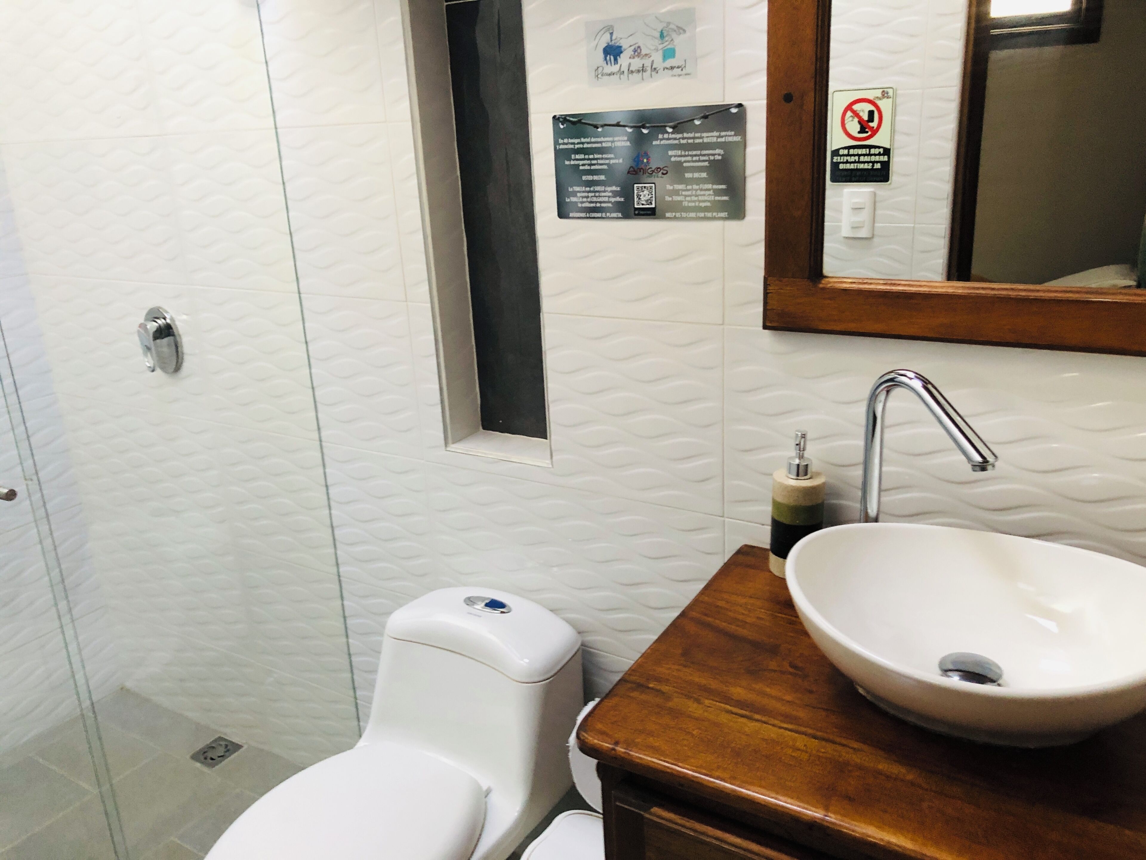 A bathroom with a white toilet, a sink with a wooden countertop, a mirror, and a wall-mounted sign.