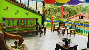 A patio with a wooden bench, chairs, and tables, surrounded by colorful walls and potted plants.