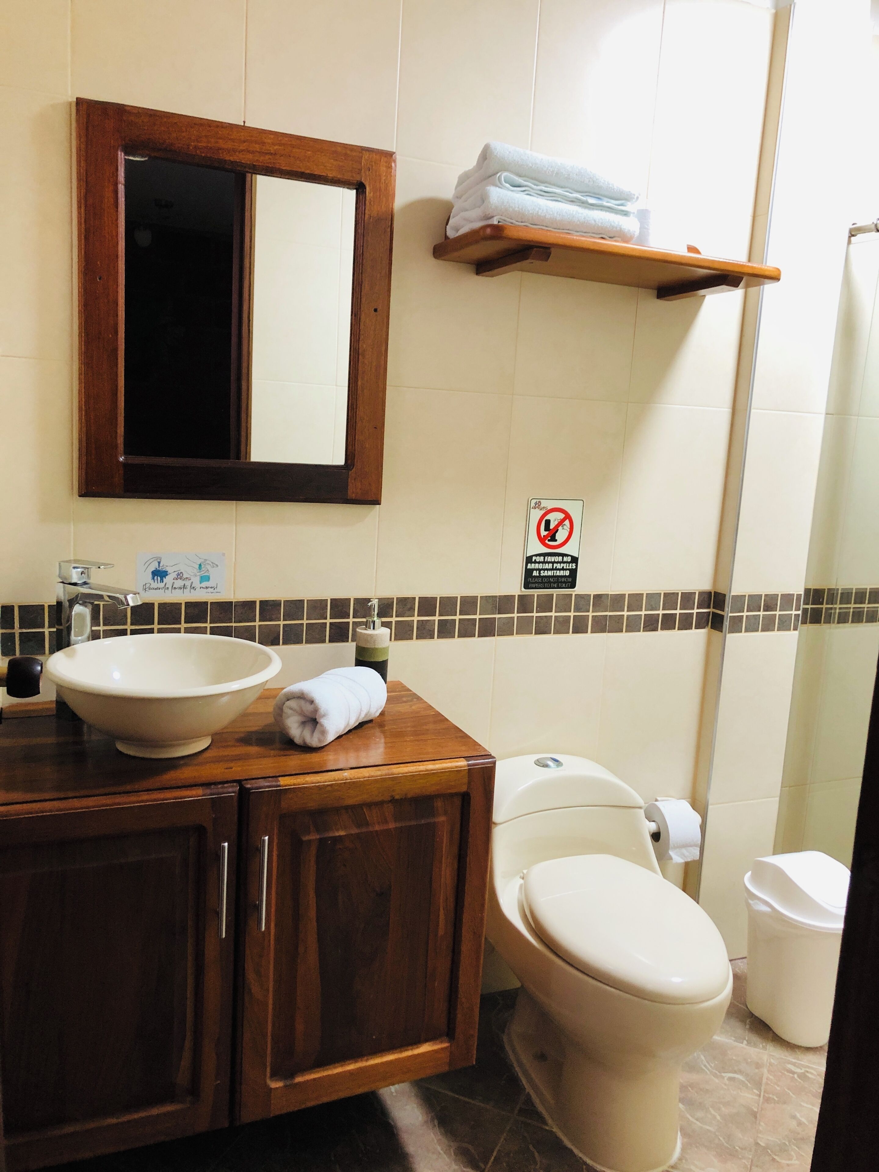 Un baño con tocador de madera, lavamanos, inodoro y espejo.