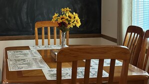 A dining area with a chalkboard wall featuring a mountain drawing and the text 'Welcome to The Mountain House.' A wooden table with chairs is set, and a vase with yellow flowers is on the table. - Mountain House - Mt. Rainier Cabin - Hot Tub, Fire Pit, Pet Friendly. (Ashford)