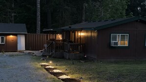 A wooden cabin with a porch, a gravel driveway, and a pathway with lights. - Mountain House - Mt. Rainier Cabin - Hot Tub, Fire Pit, Pet Friendly. (Ashford)