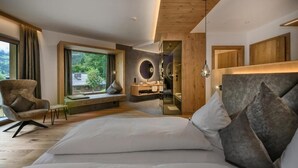 Een moderne slaapkamer met een groot bed, een stoel, een kaptafel en uitzicht op groen.