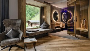 Een moderne woonkamer met een groot raam, een bank, een klein tafeltje en een glazen kast met houten planken.
