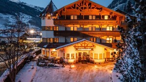 Een meerlaags hotel met een skilift op de achtergrond, een overdekte ingang en een besneeuwd landschap.
