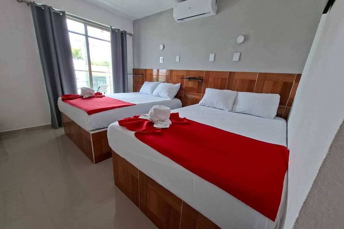 A hotel room with two beds, a wooden headboard, an air conditioning unit, and a window with curtains.