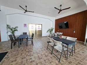 A spacious indoor area with two ceiling fans, a large TV mounted on a wooden wall, and a tiled floor.