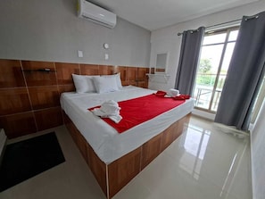 A hotel room with a large bed, a wooden headboard, a window with curtains, and a small balcony. - Hotel Regina (Centla)