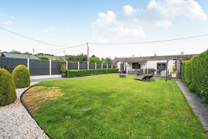 A backyard with a lawn, a barbecue area, and a small building.