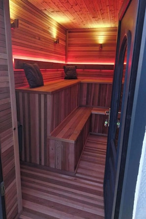 Un sauna avec des bancs en bois et une banquette, un plancher en bois et une porte.