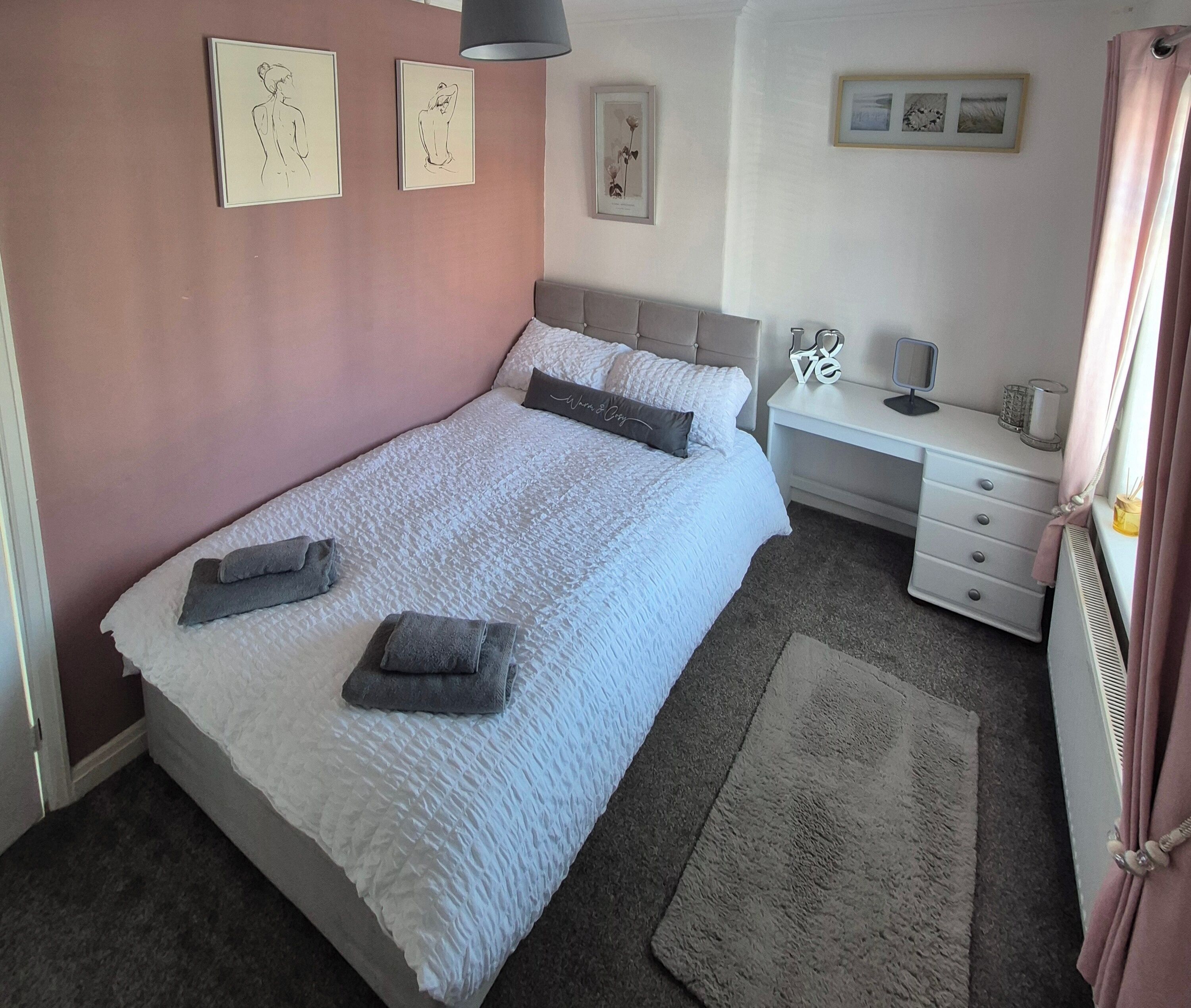 A bedroom with a bed, bedside tables, a desk, and framed artwork on the walls.