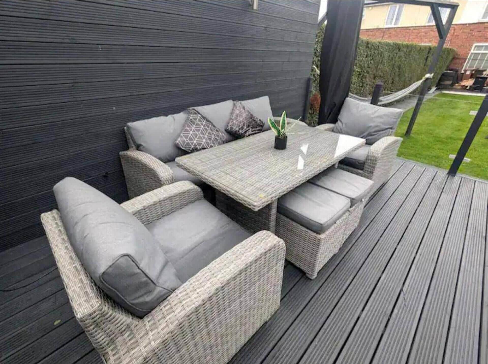 An outdoor patio with wicker furniture, a table, and cushions.