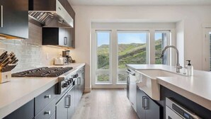 Cozinha moderna com janela ampla, eletrodomésticos de aço inoxidável e vista para o exterior.