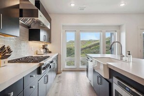 Eine moderne Küche mit einem großen Fenster, Edelstahlgeräten und Blick ins Freie.
