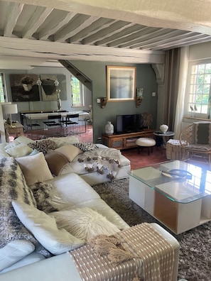 Ein geräumiges Wohnzimmer mit einem großen Ecksofa, einem Glastisch, einem Fernseher und einem Essbereich mit Tisch und Stühlen.