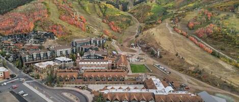 An aerial view of a hotel complex with multiple buildings, a parking area, and surrounding hilly terrain.