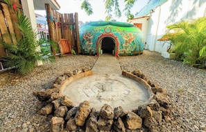 Una estructura de piedra circular con una abertura central, rodeada por una valla de madera y plantas tropicales.