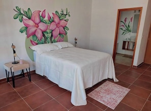 Un dormitorio con cama, mesita de noche, lámpara y un mural floral en la pared.