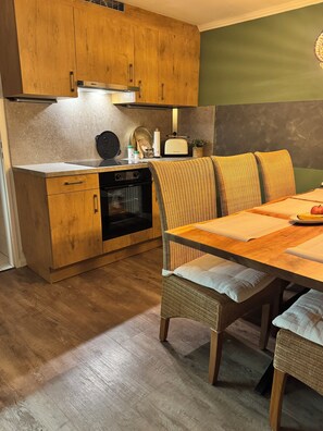 Une cuisine compacte avec des meubles en bois, un four encastré et un coin repas comprenant des chaises et une table en osier.